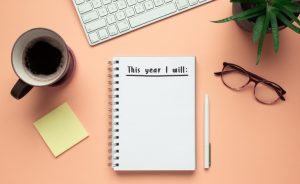 Desk with "This year I will:" notepad, keyboard, coffee, plant, glasses, and pen.