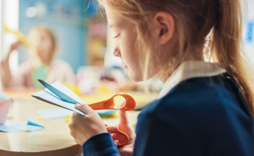 A young girl cutting paper with scissors.