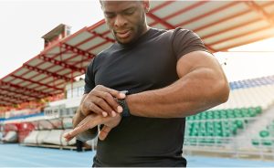 A man in a black t-shirt looking at his smartwatch outdoors.