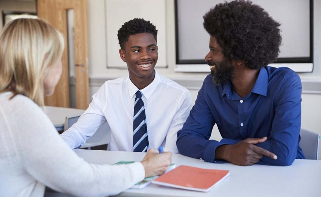 Parent-teacher conference where father and son are talking with female teacher.