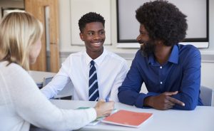 Parent-teacher conference where father and son are talking with female teacher.