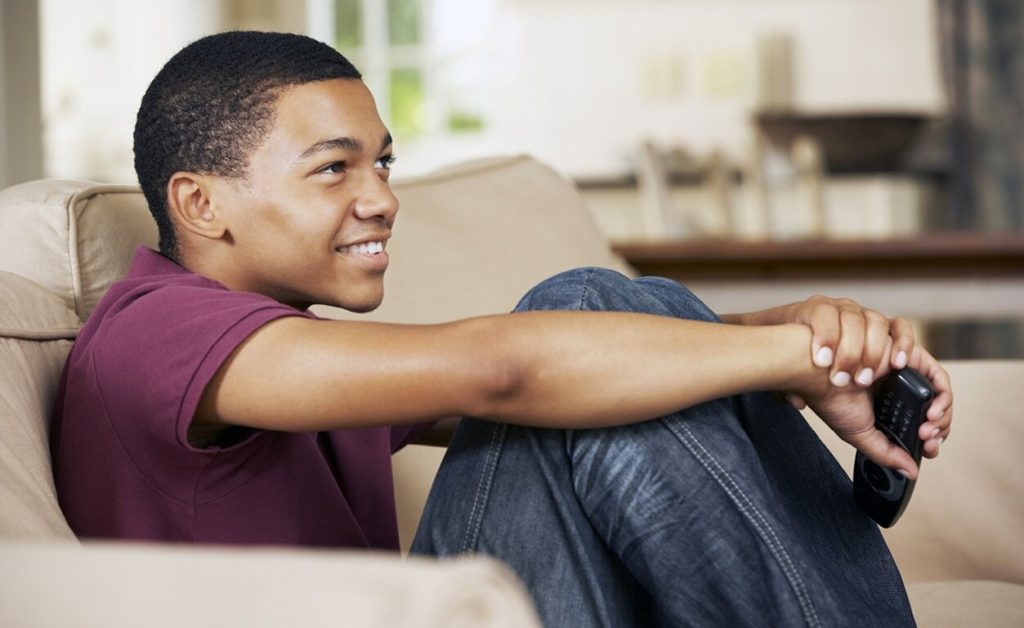 Teenager watching TV sitting on couch.