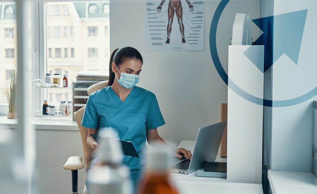 Female nurse in scrubs working on a laptop.