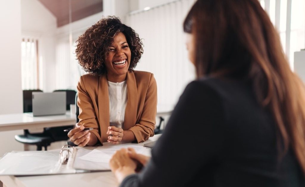 Two females engaged in a teacher interview. One is smiling and holding a pen, while the other person is facing away from the camera.