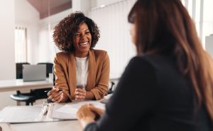 Two females engaged in a teacher interview. One is smiling and holding a pen, while the other person is facing away from the camera.