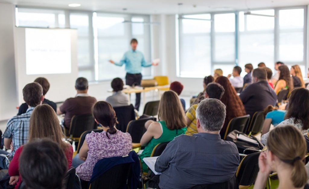 Audience listening to a speaker in a bright room.