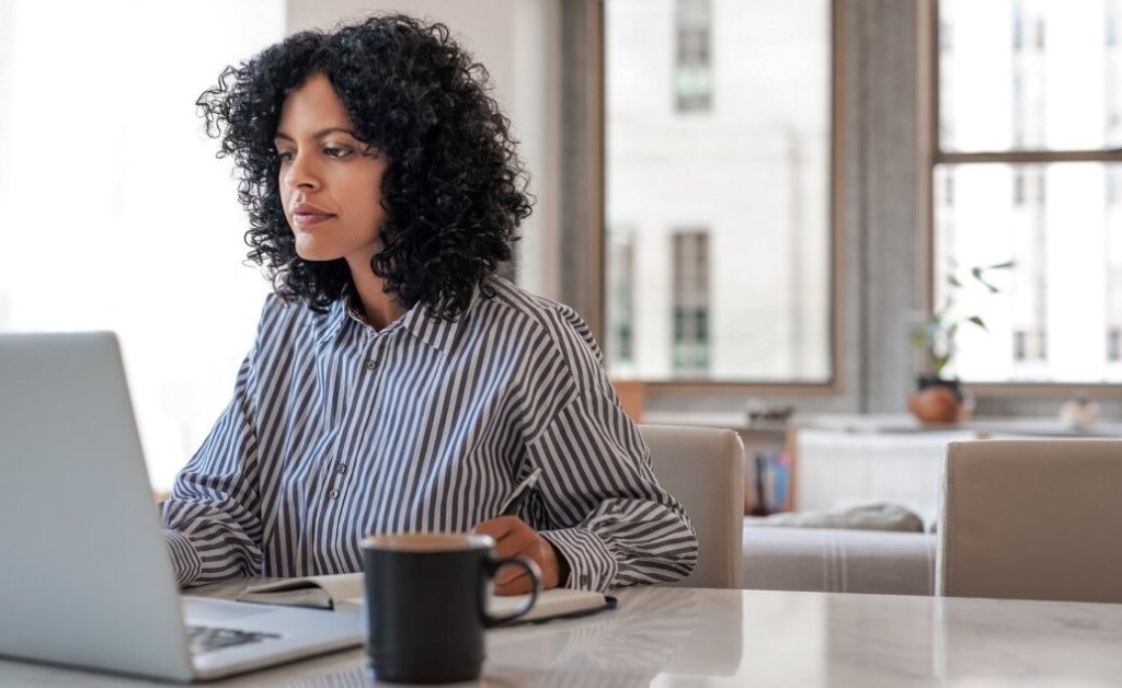 A woman with curly hair works on a laptop at a table.