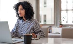 A woman with curly hair works on a laptop at a table.