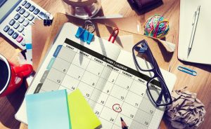 Open planner with calendar, office supplies, and coffee on a wooden desk.