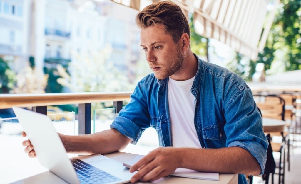 Male using a laptop outdoors during summer.