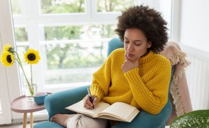 Female writing in a notebook indoors.