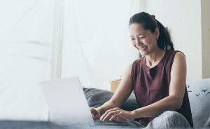 A woman smiles while using a laptop on a couch.