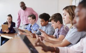 Students using tablets in a classroom with a teacher.
