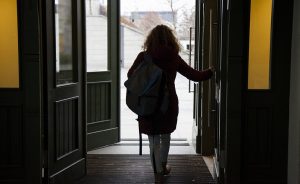 A woman with a backpack walks through an open doorway into a building.
