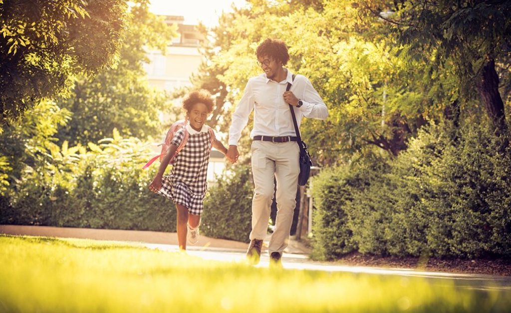 Father and daughter walking hand-in-hand outdoors on the way to school.