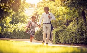 Father and daughter walking hand-in-hand outdoors on the way to school.