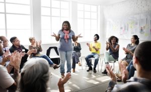 A person in a leadership role is speaking to a group of people who are clapping during a meeting.