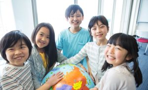 A group of smiling children gather around a globe.