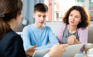 Female teacher speaking to mom and son during parent-teacher conference.