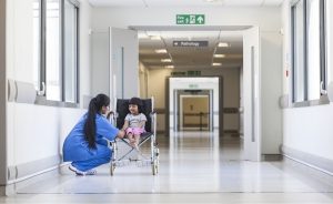 Nurse bending down talking with a child in a wheelchair in a hospital.