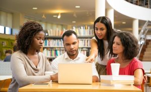 Four people working on a laptop in a library.