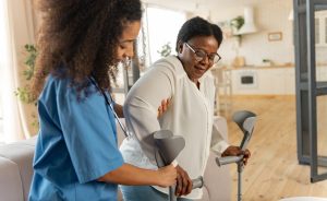 A nurse assisting a patient at home with crutches.