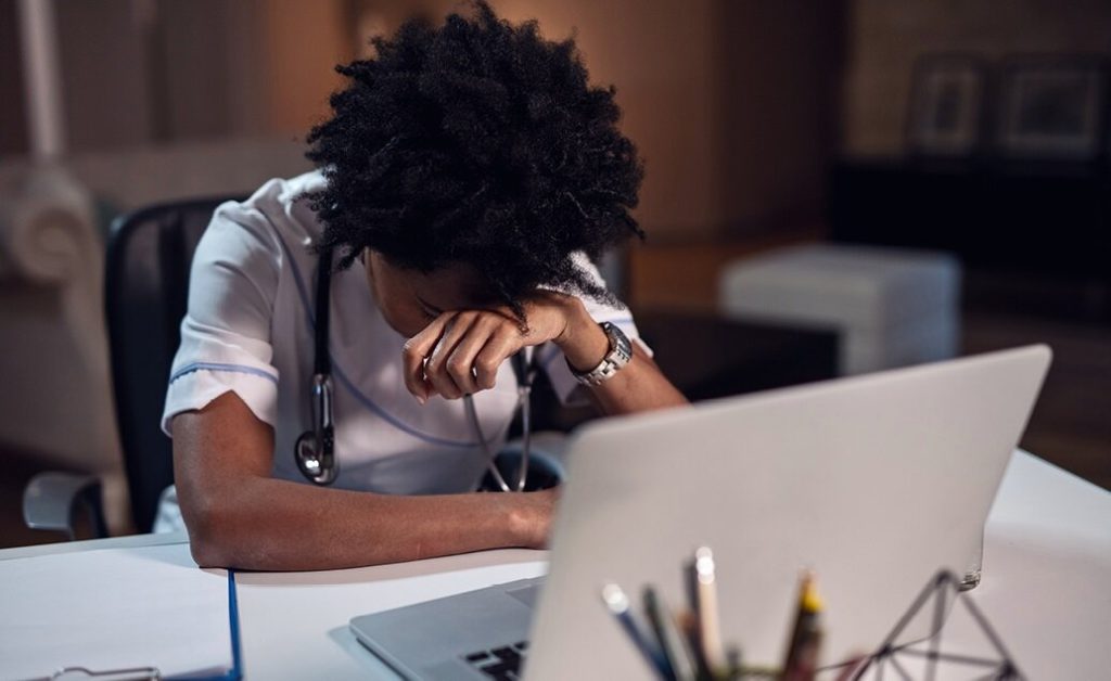 Nurse appearing to experience burnout at work while sitting at desk with a laptop