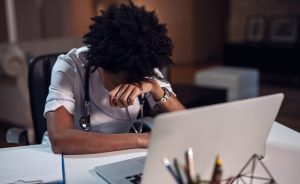 Nurse appearing to experience burnout at work while sitting at desk with a laptop