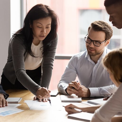 Female leader explaining a concept to group of coworkers sitting around a table.