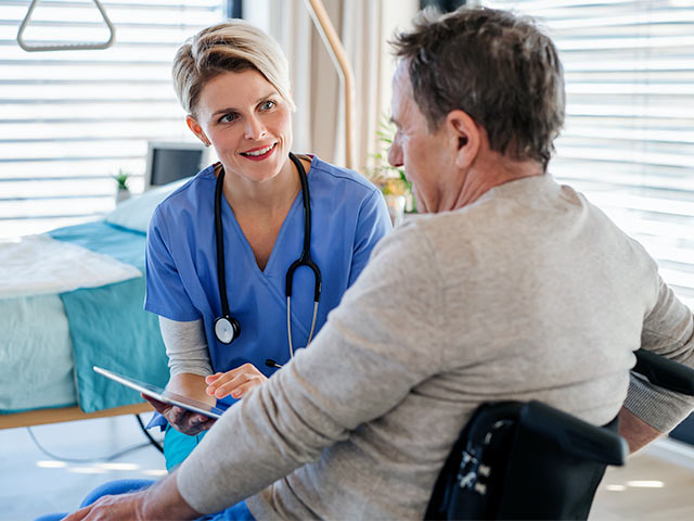 Female nurse speaking with older male patient while taking notes on a tablet.