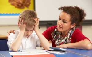 Female educator crouched next to a student holding his head in his hands in frustration