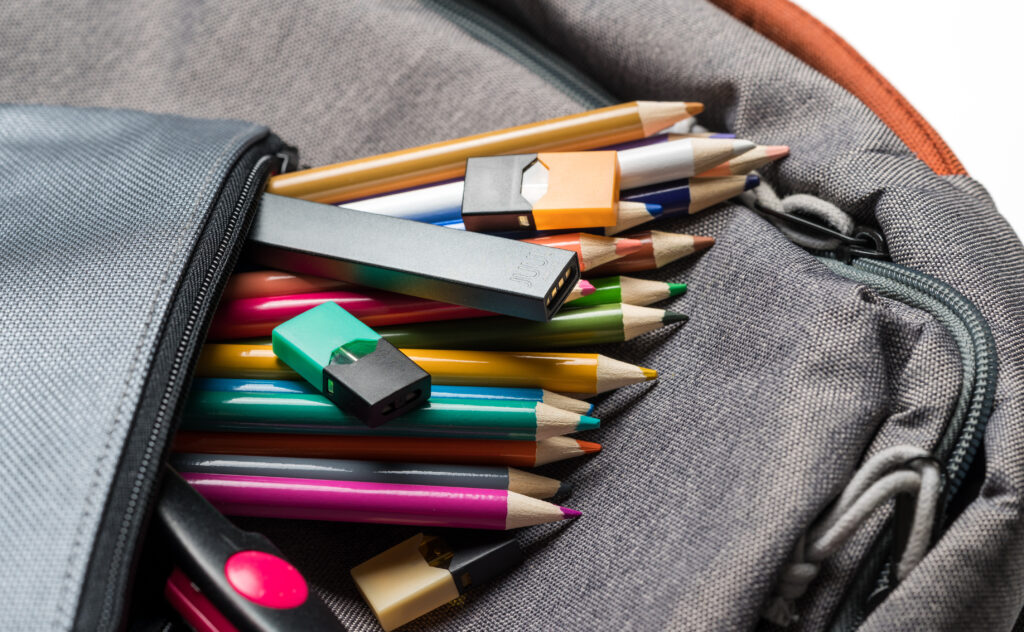 E-cigarette devices among colored pencils in a student's backpack, indicating potential youth vaping.