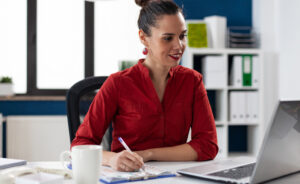 Female student taking notes at laptop.