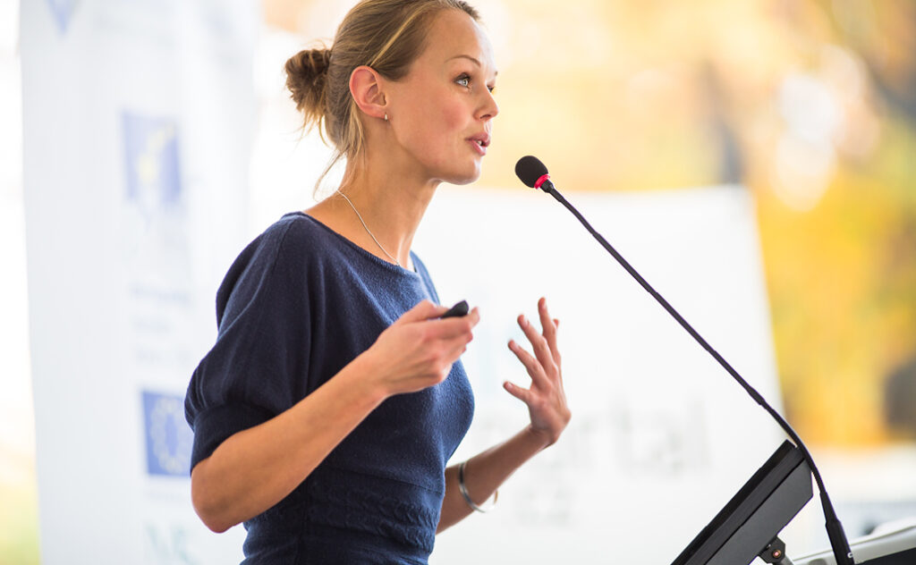 Female presenting powerpoint while speaking into a microphone.