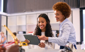 African American female teacher helping an African American female student learn on an iPad.