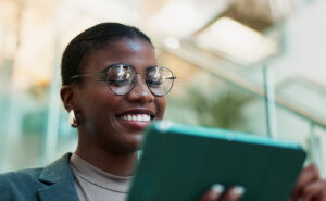 Black woman wearing glasses smiling as she looks at a tablet